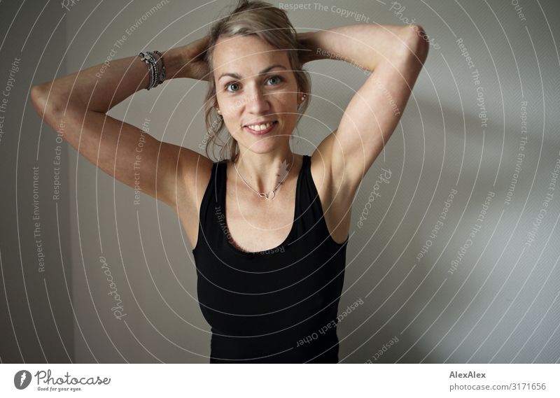 Portrait of a blonde, long-haired woman holding her hair behind her head and standing in front of a white wall Style Joy pretty Life Well-being Woman Adults