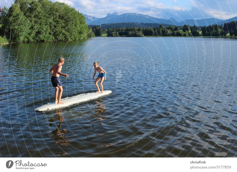 Children play on surfboard in mountain lake Leisure and hobbies Playing Children's game Vacation & Travel Trip Aquatics Swimming & Bathing Surfboard Human being