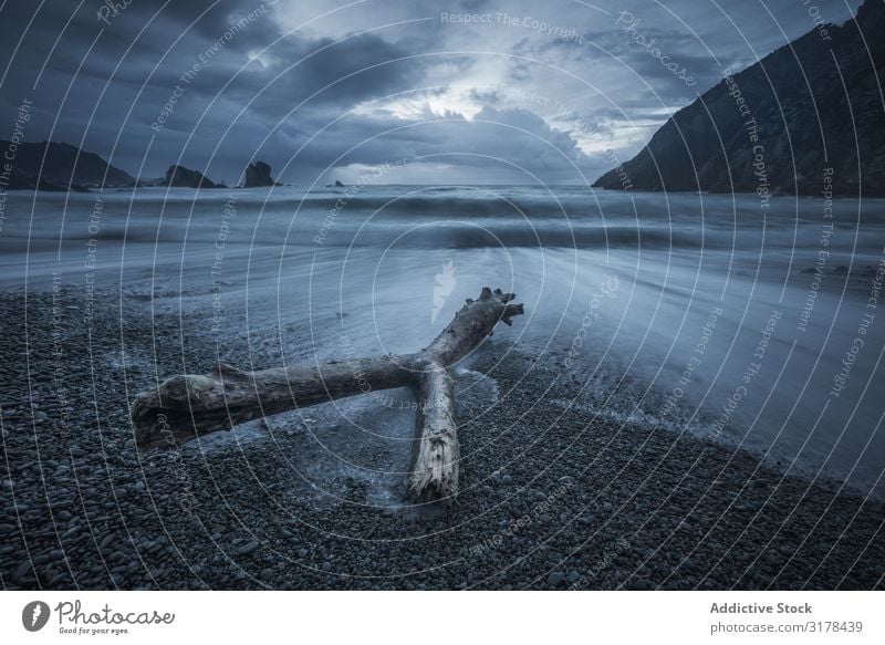 Log lying on stony beach around waves Beach Coast Gloomy Wave Stony Cliff Sky Driftwood Spain Rain spectacular Vantage point Splashing snag Nature Ocean