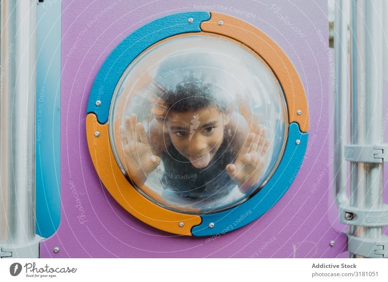 Funny black boy behind porthole on playground Boy (child) Playground Grimace Porthole Happy Action Joy Looking away Child siblings Black Ethnic African-American