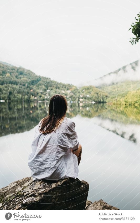 Woman sitting on rock near lake and mountains Sit Rock Lake Mountain Picturesque Water Coast Surface Amazing Vantage point Hill Stone Sky Clouds Glade Summer