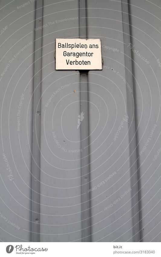 Text, lettering, notice, warning, ban: Playing ball to the garage door forbidden, written on a white sign, signboard on a grey garage door made of sheet metal, a garage in the city, by an evil, unfriendly, child-hostile neighbour.