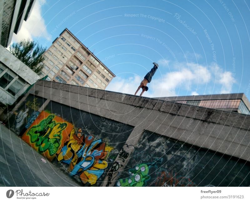 Young man doing a handstand on a high wall Lifestyle Sun Sports Human being Man Adults 1 Sky Street Graffiti Movement Fitness Effort Parkour Handstand