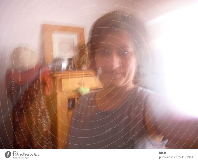 Brunette young woman at home in the living room of the apartment, behind it a wooden wardrobe, decoration, tailor's dummy. Blurred front view of woman in motion with bright light from the window with motion blur. Upper body of the adults at Selfie.