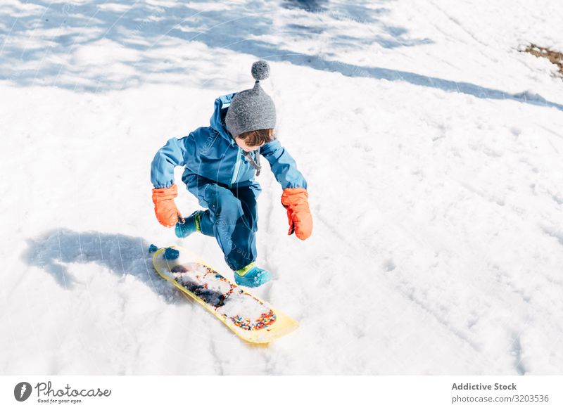 Kid jumping on board riding down snowy mountain Boy (child) Board Snow Slide Speed Small Winter Ride Sports Downward Action Relaxation Playful Jump Joy