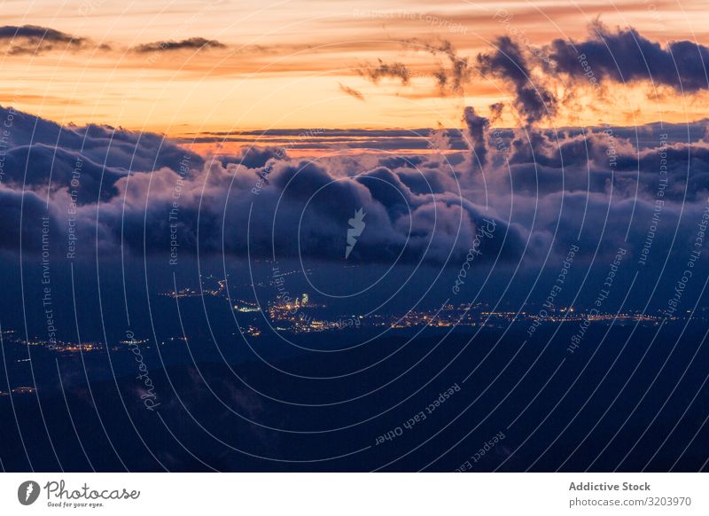 View of glowing city below clouds in sunset Landscape Sunset Clouds City terrain Mountain Valley Remote Sky Nature Dark Haze Picturesque Beautiful Vantage point