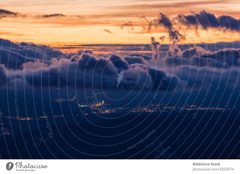 View of glowing city below clouds in sunset Landscape Sunset Clouds City terrain Mountain Valley Remote Sky Nature Dark Haze Picturesque Beautiful Vantage point