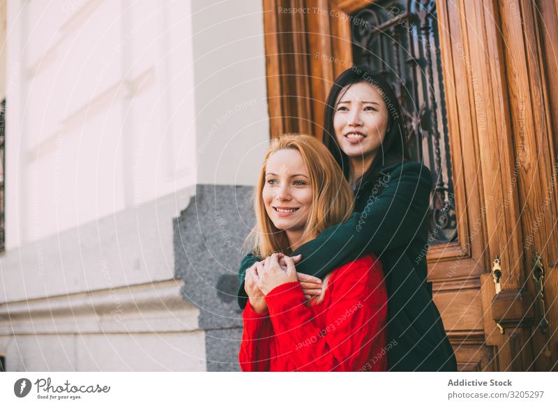 Cheerful female friends hugging near ornamental door Friendship Embrace Smiling Looking away Door Street Building City Mixed race ethnicity Together Woman