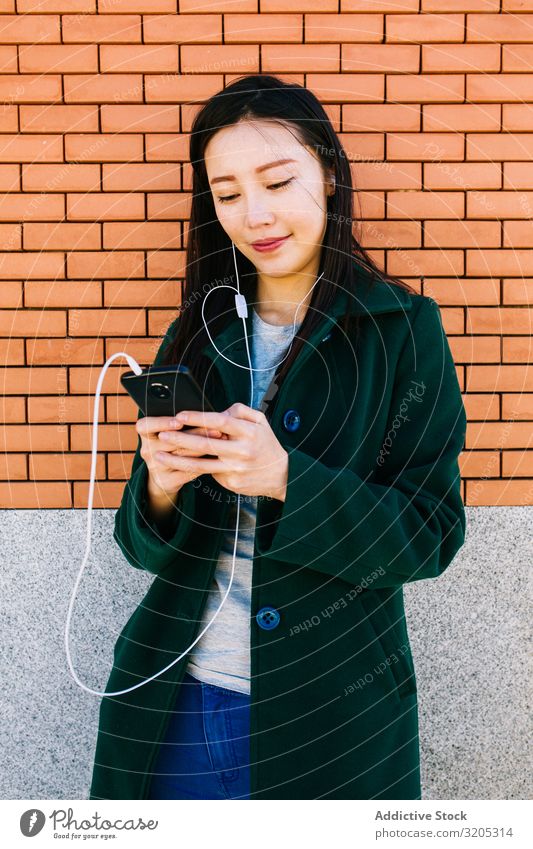 Asian female listening to music near brick wall Woman Listening Music PDA using Wall (building) Lean Brick Street City asian Ethnic Lifestyle