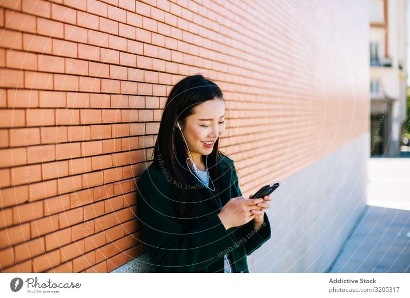 Asian female listening to music near brick wall Woman Listening Music PDA using Wall (building) Lean Brick Street City asian Ethnic Lifestyle