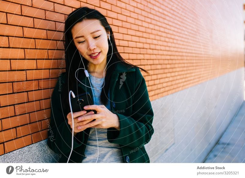 Asian female listening to music near brick wall Woman Listening Music PDA using Wall (building) Lean Brick Street City asian Ethnic Lifestyle