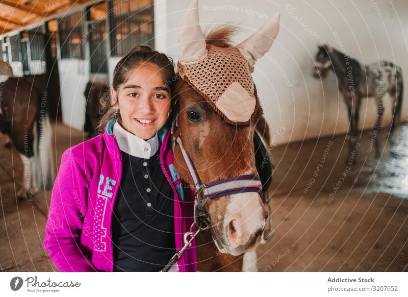 Girl with adorable pony in hat girl stable animal looking at camera child portrait embrace friend pet childhood countryside stroke little cute charming kid farm