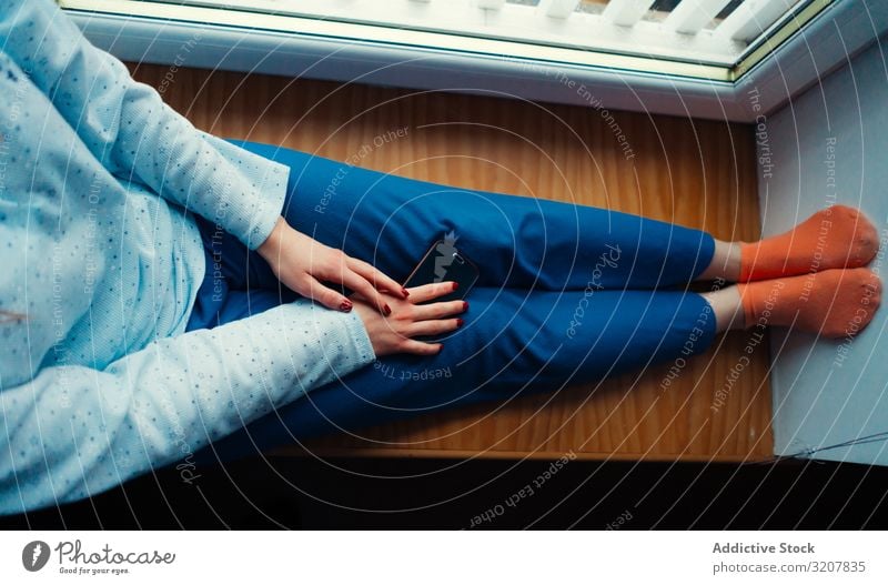 Crop woman in home clothes on window sill comfort cozy smartphone colorful scotland sitting relax lifestyle beauty candid beautiful leisure apartment device