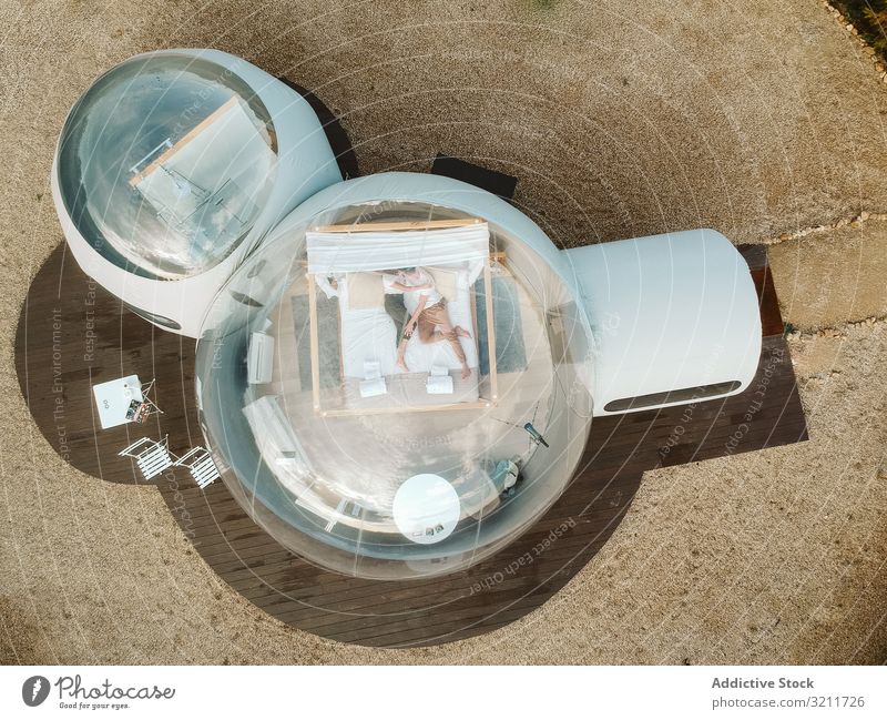 Passionate couple on bed in bubble hotel unusual affection passion love romantic kissing adventure vacation travel trip glamping young people lying hugging