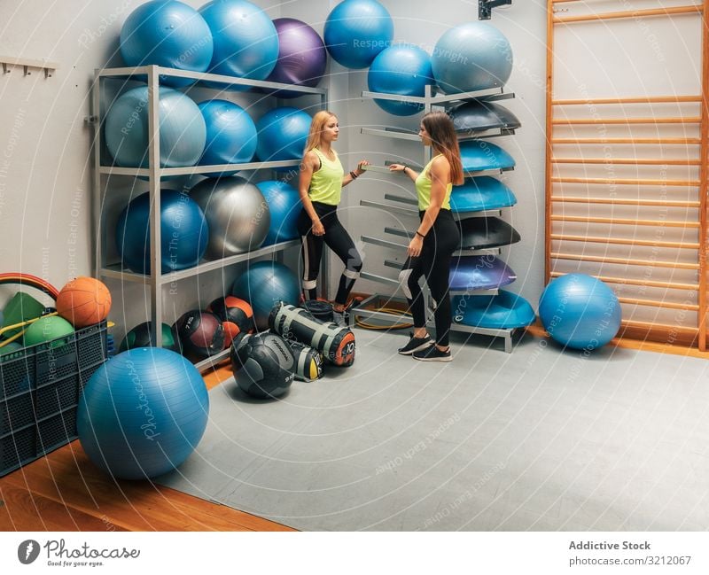 Sportswomen standing near equipment rack in gym sportswomen modern break workout center team club ball class motivation strength sportswear wellness interior