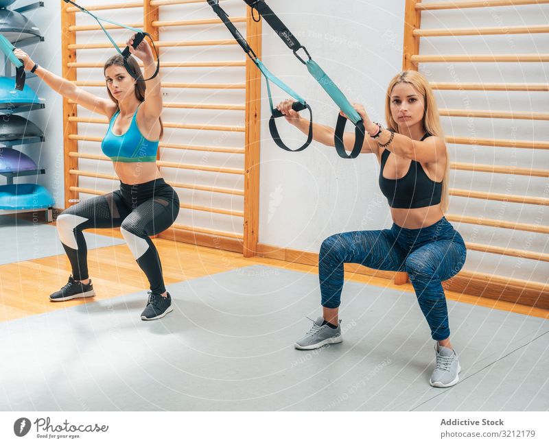 Strong ladies squatting with ropes sportswomen training suspension fitness athlete exercise trx wellbeing determination equipment sportswear gym workout