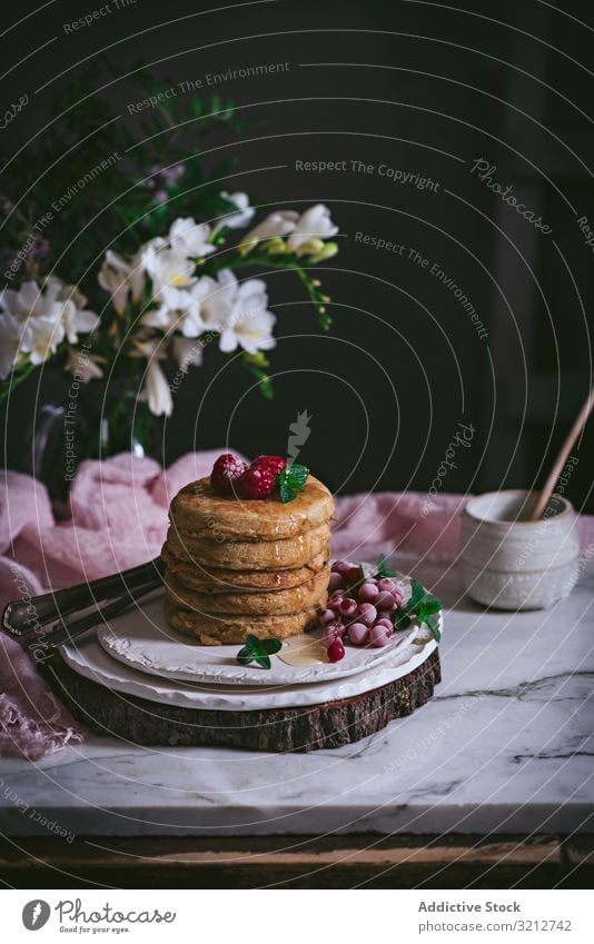 Pile of raspberry pancakes with honey on plate fresh pile golden brown stack marble porcelain tabletop flowers breakfast tasty utensil leaves stylish white