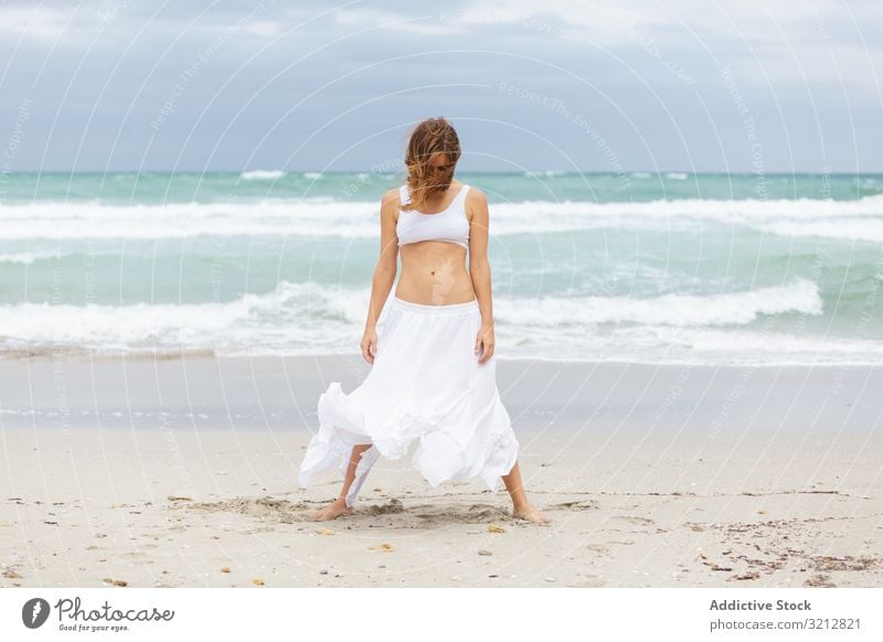 Beautiful woman dancing near sea sand shore freedom concept nature waves weather female movement posture white outfit coast beach ocean water carefree lady