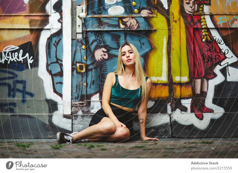 Stylish woman in sunglasses posing at graffiti wall on city street. stylish urban sitting portrait attractive beauty trendy lifestyle pretty fashion young model