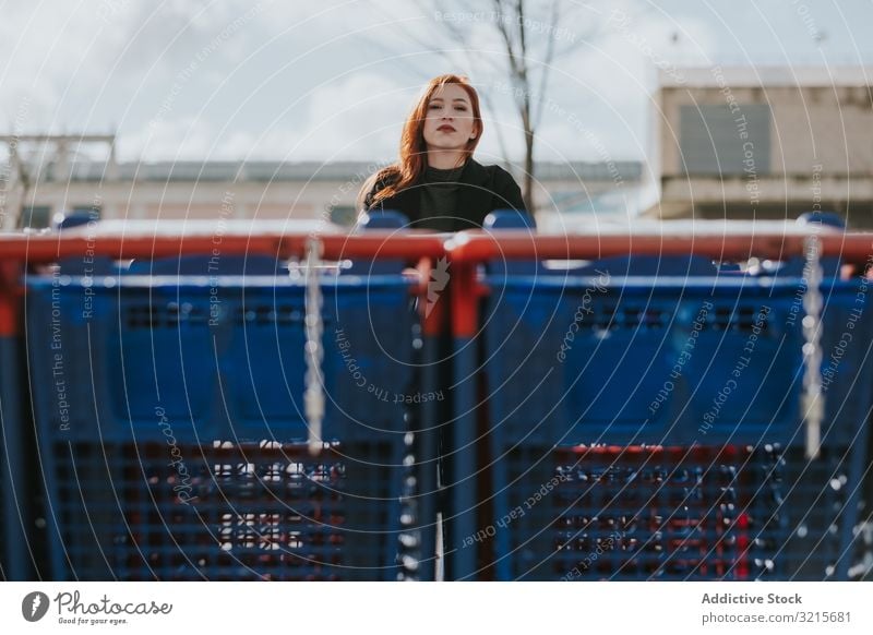 Woman standing behind blue shopping carts woman thoughtful attractive young beautiful casual smart modern redhead thinking female pretty mobile pleasure stylish