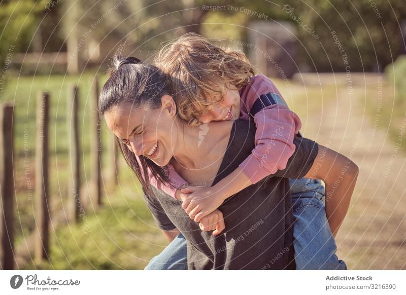 Smiling mother keeping adorable son on back countryside joyful standing happy kid little cheerful together parenthood childhood fun smiling casual nature