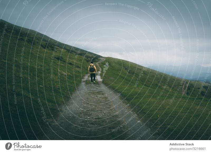 Anonymous traveler standing on road on hillside man countryside cloudy sky narrow rough grass green nature slope landscape rural scenic terrain path way track