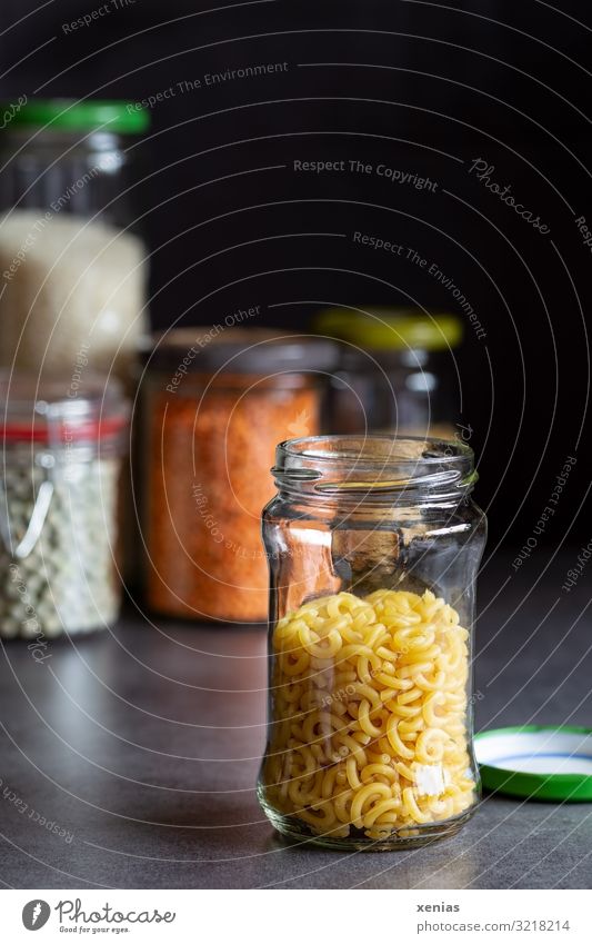 open glass container with pasta stands on a grey smooth worktop Food Grain Dough Baked goods Noodles Peas Lentils Nutrition Glass Screw top Glass container