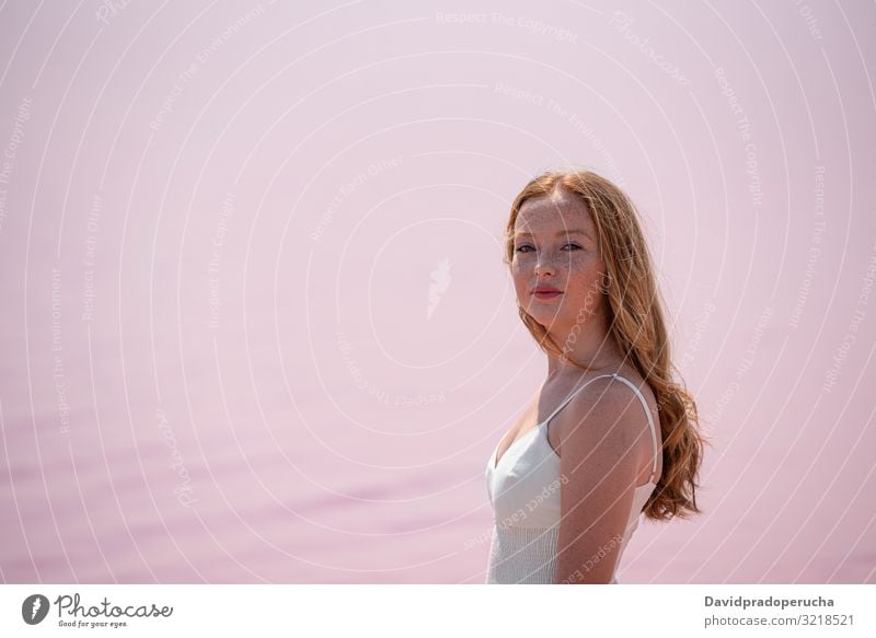 Side view of cute teenager woman wearing summer clothes standing on an amazing pink lake young romantic white freckles happy alone sea colorful adolescent water