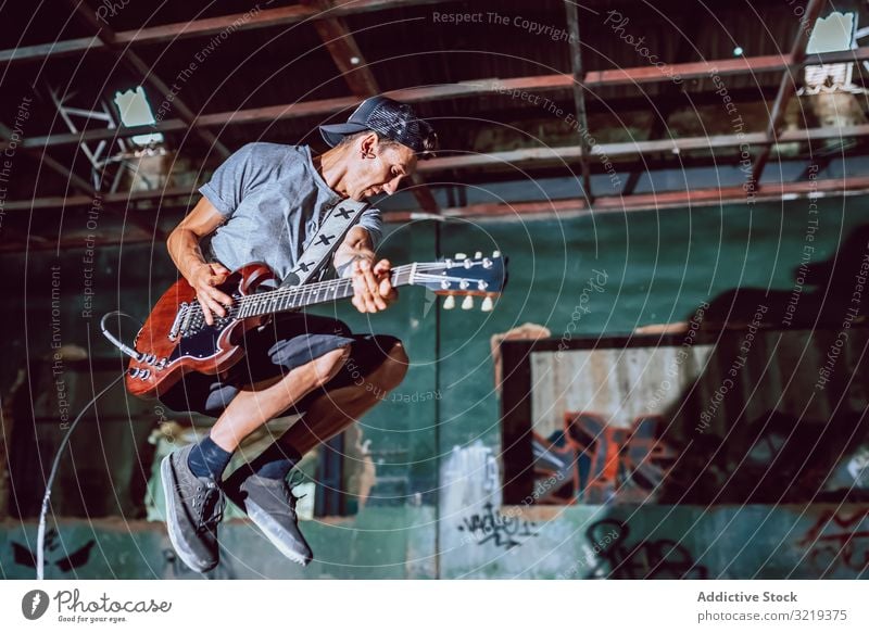 Musician playing electric guitar in abandoned place man musician jump grunge metal performance graffiti heavy rebel instrument young entertainment broken dark