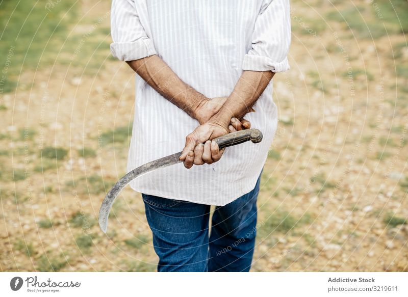 Man with sickle walking along field man casual dry farmer worker adult neat hand village nature green grass countryside cultivation agriculture summer sunny day