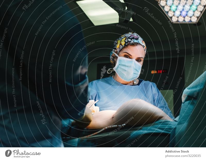 Concentrated female surgeon at work woman doctor surgery hospital operation medicine profession concentration young serious attentive surgical gown blue cap