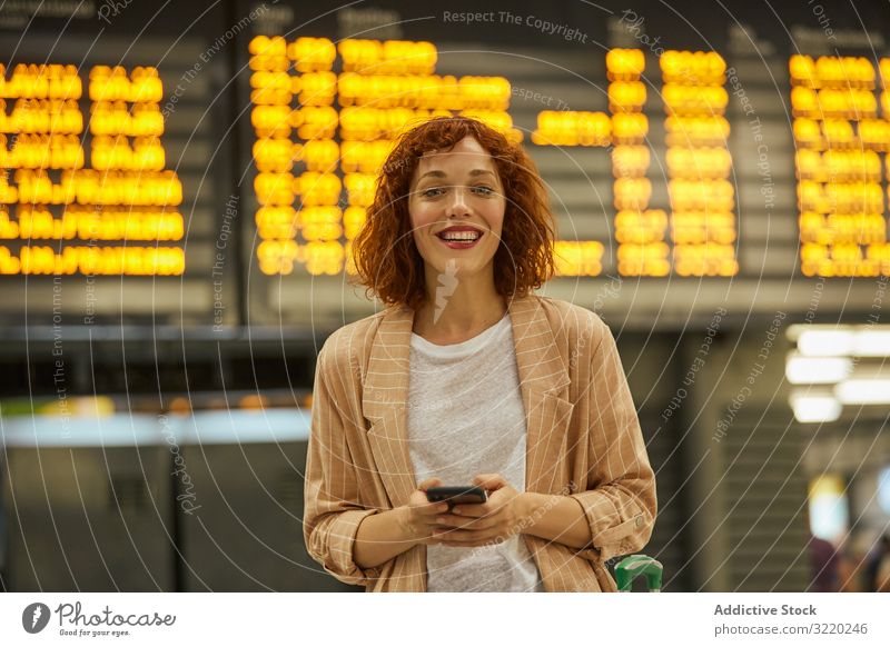 Red haired young woman using smartphone at station travel business vacation smile tourist railway departure suitcase passenger female terminal waiting schedule