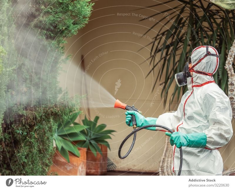 Fumigator in white uniform spraying substance on garden man fumigator trees bushes respiratory pesticide poison insect disinfection yard fumigation mask plant