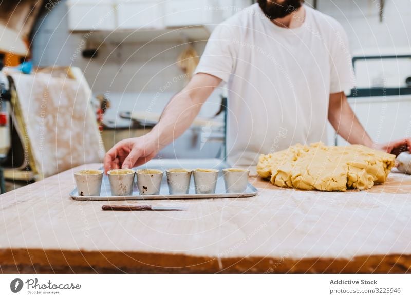 Bearded confectioner putting dough into cup bakery table kitchen pastry preparation fresh man raw cuisine professional food chef restaurant cafe cook recipe