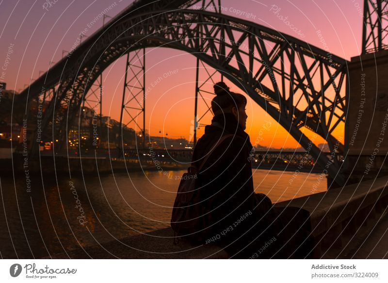 Female sitting on embankment during sundown tourist city sunset bridge river border woman water architecture landmark sky cloudless female evening dusk twilight