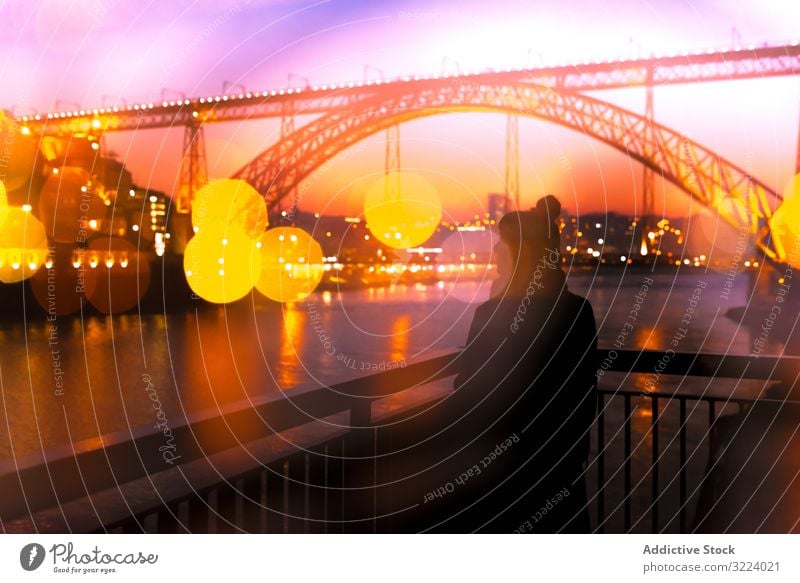 Anonymous woman standing on embankment in evening tourist city sunset bridge river border water architecture landmark sky cloudless female dusk twilight trip