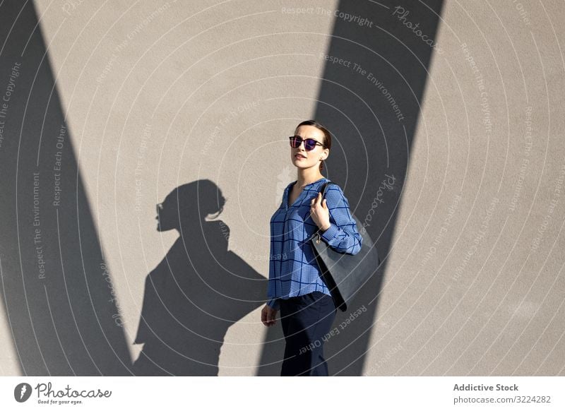 Smiling businesswoman standing near gray wall street smile city building pavement elegant modern urban female manager entrepreneur career bag sunglasses shades