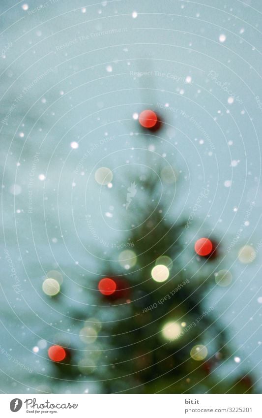 Blurred l Blurred Christmas tree with blurred light spots in the snowfall before a blue sky. Christmas tree with blurred many Christmas tree balls in red and white in the snow. Christmas in the snow, with glowing balls as decoration, ornamentation.