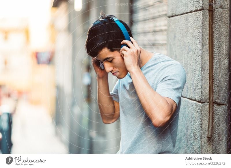 Man in headphones listening music on the street man city using streaming content cool joyful modern casual stand sunny town young adult internet online