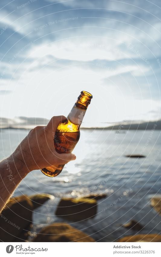 Bottle of beer in hand with seascape on background coast sunlight bottle cheers seaside alcohol beach through refreshment party travel drink tourism glass