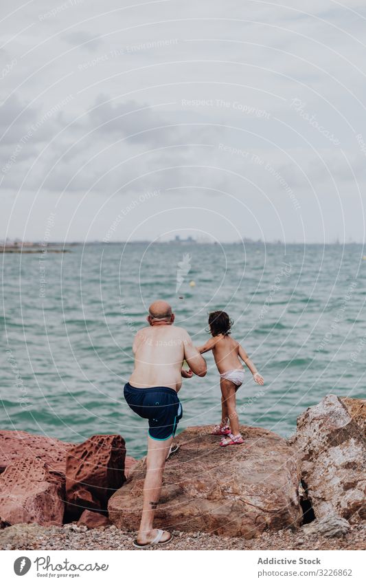 Grandfather and granddaughter having fun on rocky beach vacation grandfather ocean family elderly child girl water granddad nature shore enjoying retired