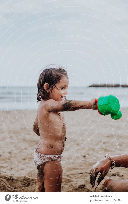 Smiling girl playing with water on sand sandy beach pouring watering summer watering can vacation together family child holiday fun sea smiling ocean person