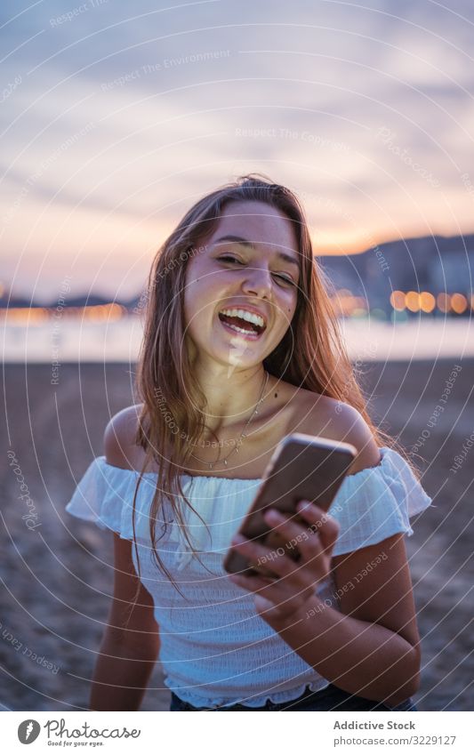 Cheerful young woman using smartphone on resort beach social media smile evening vacation summer female browsing device gadget mobile lifestyle relax rest lady