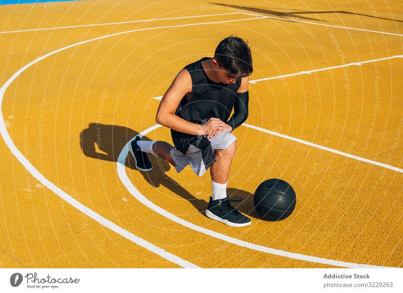 Young man and ball stretching on basketball court outdoor athlete competition sports equipment adult recreation action active activity asphalt athletic city