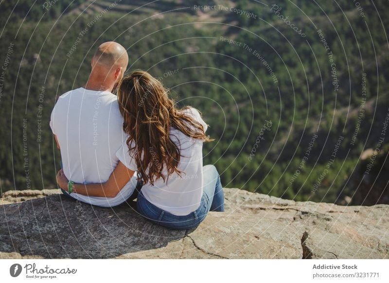 Happy couple sitting at mountain cliff freedom romantic relaxed enjoying edge height matching identical young adult recreation love lifestyle adventure vacation