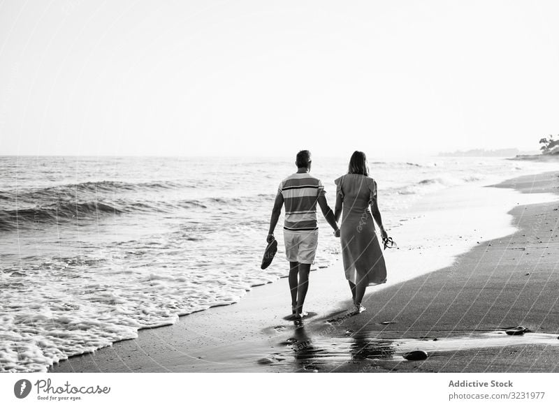 Adult couple walking towards sea beach sand wave resort together holding hands vacation man woman adult barefoot honeymoon weekend water ocean happy holiday