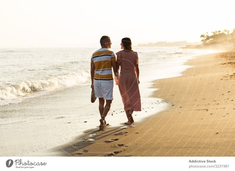 Adult couple walking towards sea beach sand wave resort together holding hands vacation man woman adult barefoot honeymoon weekend water ocean happy holiday