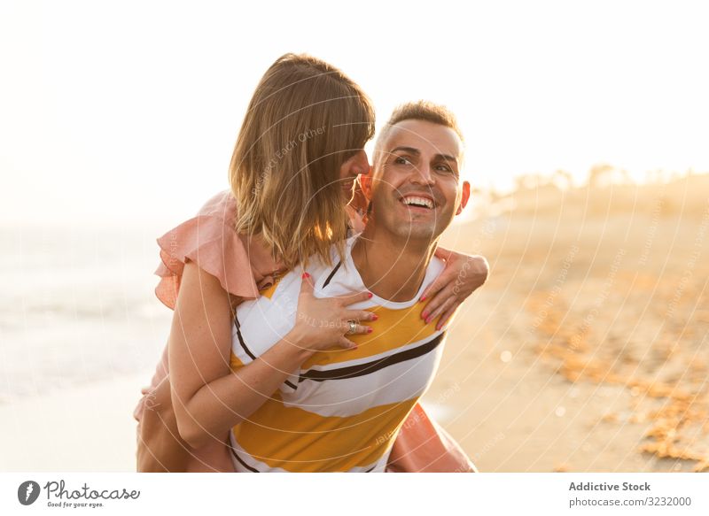 Man carrying woman on back near sea couple beach resort love piggyback ride smile happy vacation fun wave ocean water adult honeymoon summer shore coast