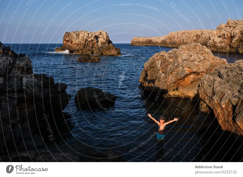 Active kid in diving mask standing in sea water boy ocean cliff rock dive picturesque arms raised shore surface seashore summer boulder journey travel lifestyle