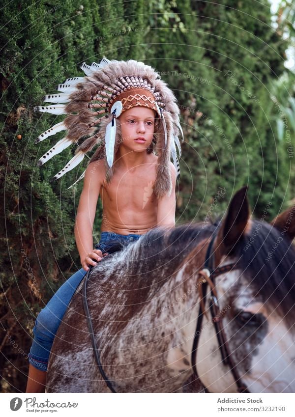 Concentrated child saddling stallion boy horse ride authentic saddle war bonnet indian costume training concentrated native art serious headdress head wear hat